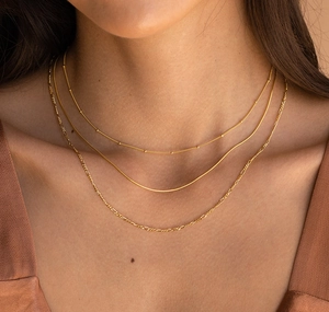 Détail de trois colliers superposés dorés avec chaînes à billes, serpent et figaro