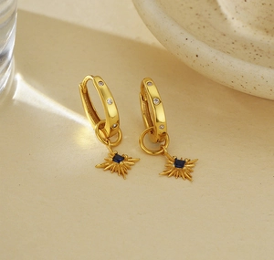Dettaglio macro di orecchini a stella dorati con zaffiro blu e pavé di diamanti