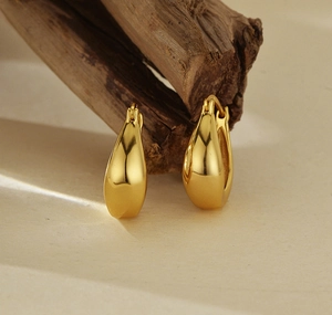 Polished golden U-shaped drop earrings displayed on a textured ceramic dish