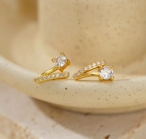 Détail macro de boucles d'oreilles dorées en V avec cristaux sur fond en céramique