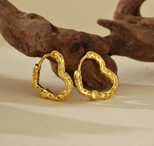 Détail de boucles d'oreilles cœur dorées avec texture lave sur support en bois