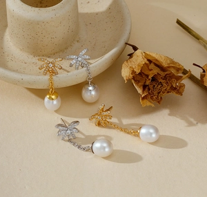 Dettaglio di orecchini a fiocco con perle pendenti in oro e argento su base beige