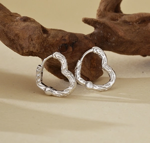 Détail de boucles d'oreilles cœur argentées à texture irrégulière sur support bois