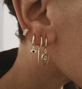 Macro detail of stacked gold earrings with blue eye pendant and pavé spiked charms