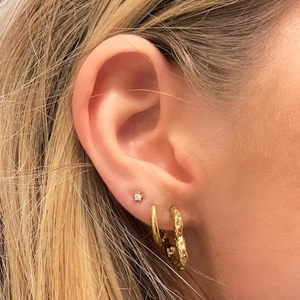 Détail de créoles dorées texturées et de puces d'oreilles avec cristaux portées