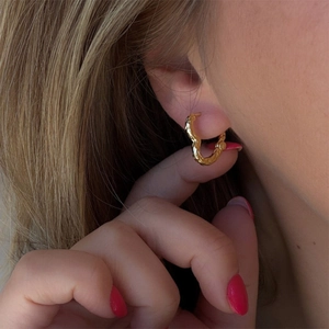 Détail de boucles d'oreilles créoles dorées à texture martelée portées par un mannequin