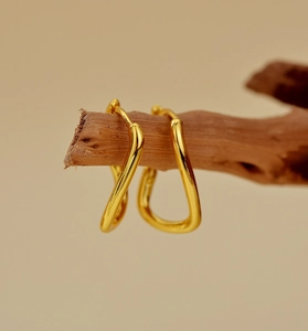 Detailed view of minimalist irregular gold hoop earrings hanging on a natural wooden branch