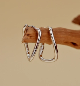 Macro shot of silver S925 geometric earrings hanging on a natural wooden branch