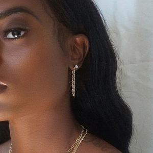 Détail de boucles d'oreilles pompon dorées en U avec diamants portées par un mannequin