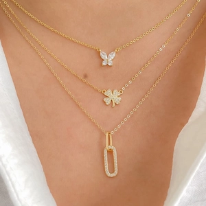 Close-up of layered gold necklaces with butterfly, clover and geometric pendants