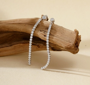 Macro shot of silver tassel earrings with zircon studs on a textured wooden stand