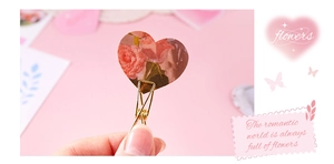 Close-up of heart-shaped gold metal clip featuring pink rose and floral butterfly patterns