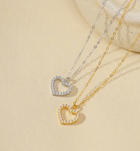 Close-up of heart pendants in gold and silver finish with pave zircon on a beige surface