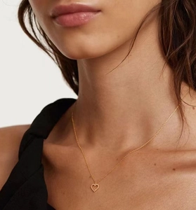 Close-up of a gold-toned hollow heart pendant necklace with beaded edges worn by a model