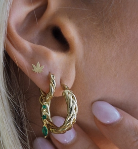 Gros plan de boucles d'oreilles dorées avec pierres vertes et détail de feuille de chanvre