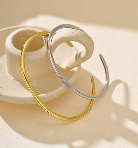 Close-up of gold and silver S925 sterling silver minimalist open bracelets on a ceramic base