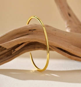 Close-up of minimalist gold-plated cuff bracelet on a natural wood branch backdrop