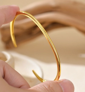 Close-up of a high-polished golden minimalist open bangle bracelet in a hand