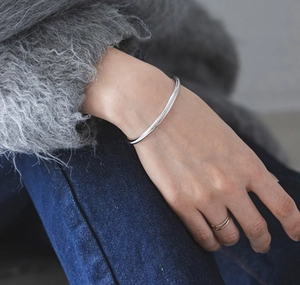 Polished S925 silver open bangle with minimalist rings on a soft textile background