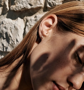Close-up of minimalist square-cut zircon stud earrings worn on ear with gold plating