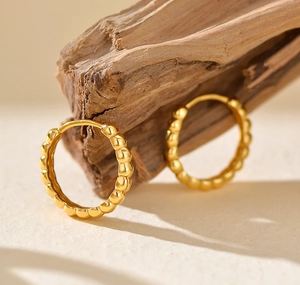 Macro shot of gold beaded huggie earrings with a textured bubble design on wood