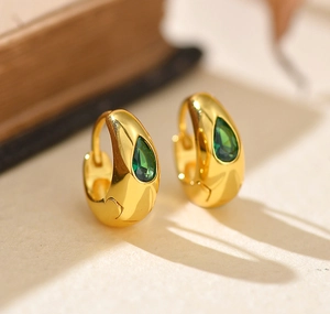 Détail macro de boucles d'oreilles créoles dorées avec zircons verts en forme de poire