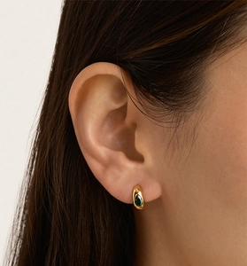 Gros plan de boucles d'oreilles dorées avec zircon émeraude portées sur l'oreille