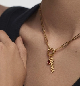 Close-up of gold paperclip chain necklace with MAMA pendant and red teardrop gem