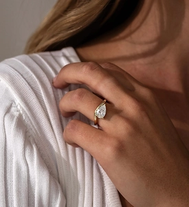 Close-up of a pear-shaped zircon ring with a wavy golden band on a finger
