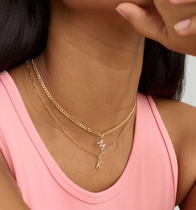 Detail of layered gold necklaces with micro-set M pendant and polished K paperclip chain