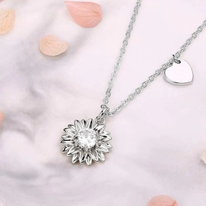 Détail du collier marguerite en argent avec zircon et breloque coeur sur fond de marbre
