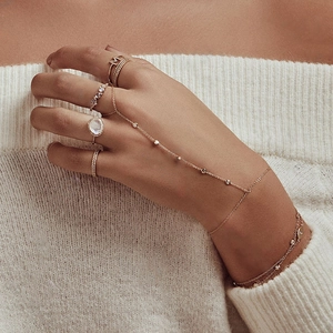 Detail of gold hand chain ring with M letter, moonstone and zircons on knitted fabric
