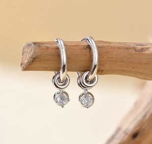 Macro shot of silver drop earrings with zircons on a wooden branch detail