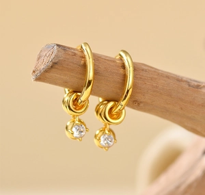 Close-up of gold hoop earrings with small charms and clear crystal pendants on wood