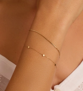 Close-up of gold layered heart charm bracelet and snake chain on model's wrist