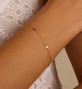 Close-up of gold heart charm bracelet on wrist with elegant white lace clothing