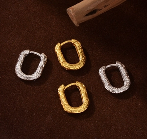 Detailed close-up of oval silver and gold hoops with a molten lava texture on brown suede