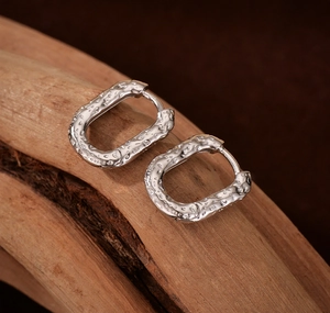 Macro detail of silver oval hoop earrings with hammered lava texture on wood stand