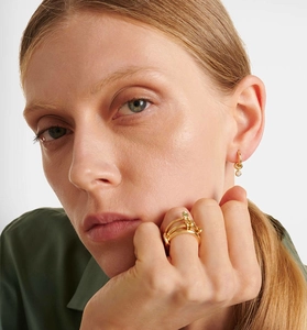 Detail of model wearing a gold multi-layer ring with green accent and small hoop earrings