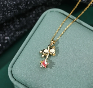 Macro detail of a 3D gold bear necklace with sparkling stones and pink aurora star charm