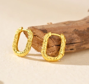 Detailed macro view of gold-plated U-shaped earrings with hammered lava texture
