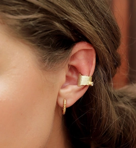 Macro shot of textured gold oval hoop earring and studded cuff on ear with vintage finish