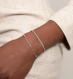Detail of silver tennis bracelet and marquise stone chain on wrist with blazer sleeve