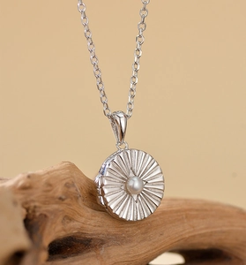 Macro shot of silver circular locket with sunburst engraving and pearl inlay details