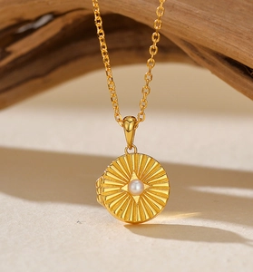 Detail of round gold locket necklace with center pearl and radial sunburst engraving