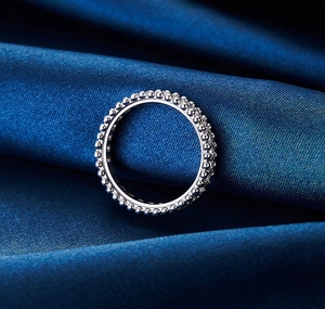 Makroaufnahme eines silbernen S925 Perlenrings auf blauem Satin mit Perlée-Handwerkskunst
