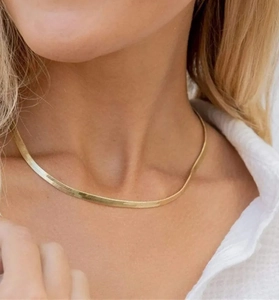 Primo piano di una collana a catena piatta dorata minimalista indossata sulla clavicola