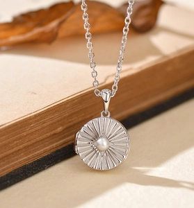 Close-up of silver starburst locket with pearl on vintage book edge and dried leaves