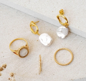 Set orecchini con perle barocche e anello dorato su superficie in pietra con fiori secchi