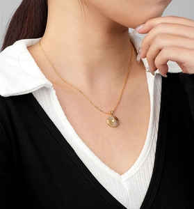 Detail view of a gold starburst locket necklace with a centered white pearl inlay